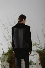 Chaleco de piel sintética en color chocolate, con cierre frontal y detalles de cuero en los bordes. Presenta un diseño de cuello solapa y ajuste lateral con hebillas.