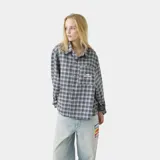 Camisa de franela a cuadros en tonos grises, negros y azules, con cuello clásico, corte ligeramente oversize, cierre frontal con botones y bolsillo en el pecho con logo bordado.