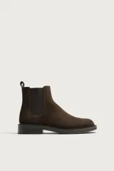 Bota chelsea de gamuza color marrón oscuro, con elásticos laterales en contraste, punta redonda y suela plana con ligero tacón.