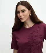 Remera de algodón con cuello redondo y mangas cortas, caracterizada por un bordado floral en relieve aplicado en el frente.