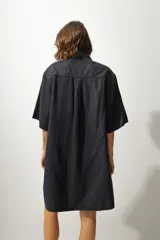 Vestido corto de denim azul, corte camisero holgado, mangas cortas amplias, cuello clásico, cierre frontal con botones, bolsillo aplicado en el pecho y pequeño bordado lateral en el dobladillo.