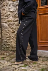 Pantalón de denim blanco de corte amplio, con cierre de botón y cremallera, y detalles de tachas en los laterales y bolsillos.