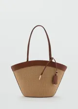 Bolso tipo shopper de tamaño grande con cuerpo de tejido trenzado en tono beige y detalles en cuero sintético marrón, incluyendo asas superiores dobles, bordes y un charm colgante.