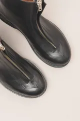 Bota corta de cuero negro con cierre frontal con cremallera y suela de goma.