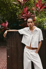 Camisa de algodón blanca con cuello solapa, manga corta y bolsillo de plastrón en el pecho. Presenta detalles de bordados a tono y cierre frontal con botones ocultos.