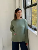 Sweater de punto color verde, de corte recto y holgado, con cuello redondo y dos bolsillos frontales aplicados.