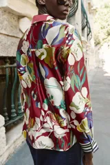 Camisa de cuello solapa y manga larga con puños a rayas. Confeccionada en tejido satinado con estampado floral multicolor sobre base roja. Cierre frontal con botones forrados.