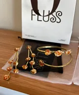 Conjunto de brazalete rígido y aros colgantes de bronce dorado, con incrustaciones de piedras irregulares en tonos ámbar con detalles de hoja de oro.