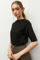 Remera negra de cuello redondo y manga tres cuartos, confeccionada en tela con textura sutil. Presenta fruncidos laterales que aportan caída y movimiento a la prenda.