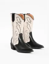 Bota corta de cuero sintético color negro y blanco, con punta fina y bordados decorativos.