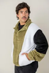 Buzo de textura afelpada con diseño de bloques de color en verde, blanco y negro. Presenta cuello alto con cierre de botones a presión y bolsillos laterales.