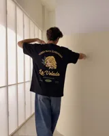 Remera negra de corte oversize con estampa gráfica en la espalda que simula un paquete de yerba mate, con ilustración de una mujer rubia y texto alusivo.