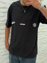 Remera negra de corte oversize con cuello redondo y manga corta. Presenta tres estampados blancos en el frente: un símbolo curvo a la izquierda, la palabra "OSTEN" en el centro y un símbolo abstracto a la derecha.