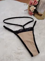 Tanga de diseño moderno confeccionada en lycra color beige con detalles de encaje negro en la parte superior. Presenta tiras elásticas ajustables en la cintura y bordes reforzados en color negro.