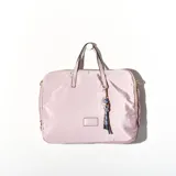 Bolso tipo tote de tela color rosa pálido, con doble asa corta y cierre superior con cremallera. Incluye un dije decorativo con cuentas de colores y flecos.