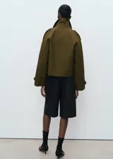 Chaqueta corta de doble botonadura en color verde militar, con cuello de solapa, bolsillos laterales, trabillas en los hombros y mangas largas con puños abotonados.
