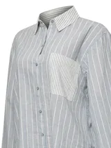 Blusa de lino y algodón orgánico modelo Lines de RKF, color celeste con rayas verticales blancas. Cuenta con cuello camisero, cierre frontal con botones, mangas largas con puños abotonados y un bolsillo aplicado en el pecho con rayas en disposición vertical contrastante.