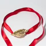 Colgante con dije dorado con forma orgánica irregular y cinta de raso roja.