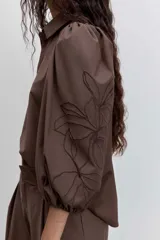 Camisa de color marrón con cuello clásico, mangas abullonadas y detalle de bordado floral en una de las mangas.