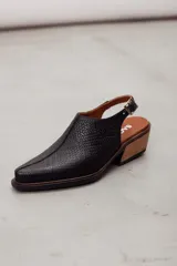 Zueco slingback negro de cuero vacuno con textura grabada geométrica, taco bloque de madera y tira ajustable con hebilla metálica.