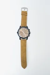 Reloj analógico con caja negra y esfera color cobre con subesferas. Correa de cuero marrón claro con costuras blancas y hebilla plateada.