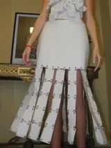 Falda larga de cuero blanco con diseño de tiras unidas mediante argollas y remaches metálicos.