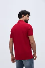 Remera polo verde militar de algodón pima, con cuello y puños acanalados, cierre frontal de tres botones y pequeño bordado de ave en el pecho.