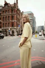 Blazer color amarillo pastel con textura, cuello solapa, manga corta con hombreras, bolsillos de vivo en delantero, forro interior y cierre frontal cruzado con botones.