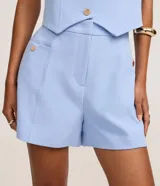 Short sastre de cintura alta, color blanco, con bolsillos laterales y detalles de tachuelas metalizadas.