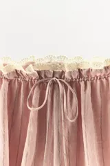 Shorts de tiro bajo en mezcla de viscosa y lino, color rosado con sutiles rayas verticales. Presenta cintura elástica fruncida con lazada frontal ajustable y aplicación de puntilla en contraste en el borde superior. Diseño de bajo abullonado tipo globo.