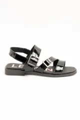 Sandalias planas de cuero negro charol con doble tira frontal ajustable mediante hebillas metálicas y tira en el talón.