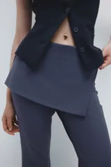 Pantalón acampanado de tiro alto con pollera mini integrada en la cintura, confeccionado en tela lisa de color gris oscuro.