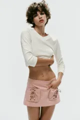 Falda mini de tiro bajo color rosado con estampado de rayas verticales. Presenta dos bolsillos de parche en el frente con detalles de cordones cruzados ajustables y cierre lateral con cremallera oculta.
