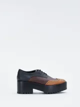 Zapato estilo brogue con plataforma y taco ancho, confeccionado en cuero bicolor con detalles perforados en la puntera y los laterales.