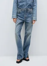 Pantalón de jean de tiro medio con diseño recto y cinco bolsillos. Presenta aberturas laterales en el bajo y cierre frontal con cremallera y botón.
