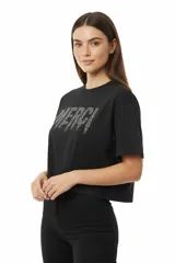 Remera de algodón negra, corte holgado y corto (cropped), con cuello redondo a la base y la palabra "MERCI" estampada con apliques de studs plateados.