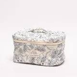 Neceser acolchado con cierre, color crema, estampado floral en azul marino. Presenta un parche textil con texto en el frente.