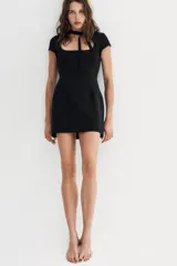 Vestido corto de color negro con escote cuadrado y detalle de lazada en el cuello. Presenta mangas cortas y cierre de cremallera oculta en la espalda.