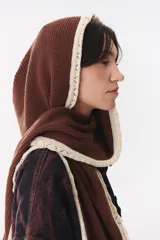 Bufanda de punto color marrón con capucha integrada y bordes en color crema. Presenta una etiqueta rectangular bordada con la palabra Anthea en uno de sus extremos.