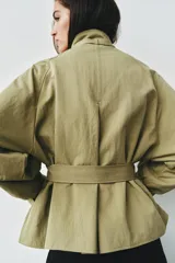 Cazadora de color verde militar, con cuello alto, manga larga abullonada con puños y cierre frontal con botones a presión ocultos. Incluye un cinturón ajustable del mismo tejido para entallar la cintura y bolsillos delanteros de vivo.