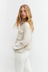 Chaqueta bomber color beige melange, de lino, con cuello mao, cierre frontal con botones a presión, dos bolsillos con solapa en el pecho y puños y cintura elastizados.