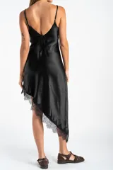 Vestido midi de satén negro con escote en V y tirantes finos. Presenta un diseño asimétrico en el ruedo con detalle de encaje aplicado.
