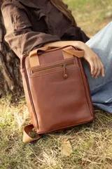 Matera mochila unisex de cuero marrón, con diseño estructurado, bolsillo frontal con cierre, asas superiores y correas ajustables.