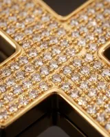 Collar de acero con baño de oro, compuesto por una cadena de eslabones y un dije en forma de cruz con incrustaciones de cristales brillantes.