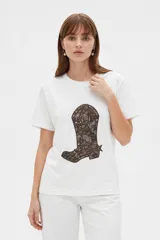 Remera blanca de manga corta y cuello redondo, con un gran estampado central en tono marrón que representa una bota vaquera con diseño paisley.