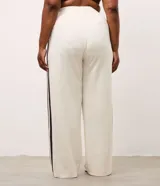 Pantalón deportivo de corte oversized estilo college, confeccionado en microfibra color crema con rayas laterales contrastantes en color marrón. Presenta cintura fija, bolsillos funcionales y frisos frontales.