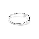 Brazalete rígido de la colección Idyllia, con diseño de media caña adornado con cristales transparentes. Presenta un dije central en forma de corazón tipo medallón, con baño en tono oro y una zirconia rosa en una cara, y pavé de cristales con baño de rodio en la otra.