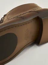 Botas de cuero marrón oscuro estilo brogue, con cordones y suela baja.