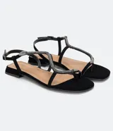 Sandalia baja Satinato, tipo chatita, de color negro con tiras adornadas con pedrería brillante y un detalle metálico en forma de serpiente. Cuenta con cierre de hebilla ajustable en el tobillo.