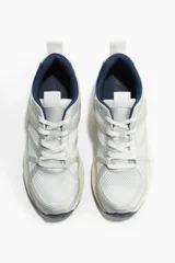 Zapatillas deportivas blancas con detalles en gris y azul marino. Capellada de malla con refuerzos sintéticos, cuello y lengüeta acolchados, cierre con cordones y suela gruesa con diseño.